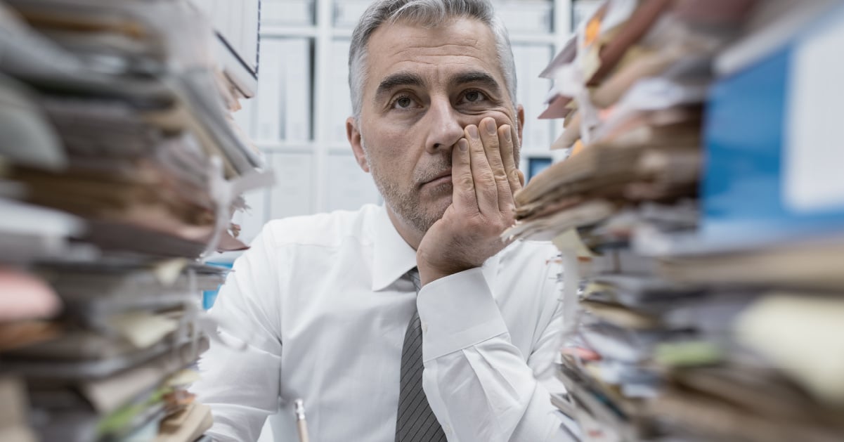 Stacks of paperwork surround an executive at a government agency involved in a messy procurement process. 