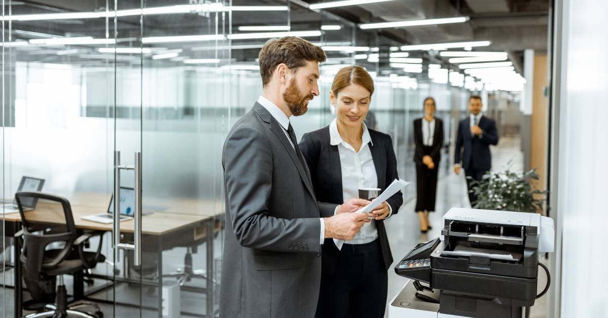Two employees picking up print jobs at office printer. 