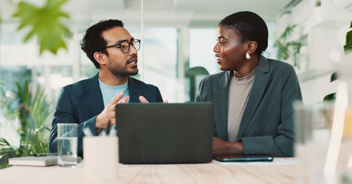 Two employees have a discussion in front of an open laptop.