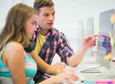 An adult tutor pointing at a computer monitor explaining something to the student.
